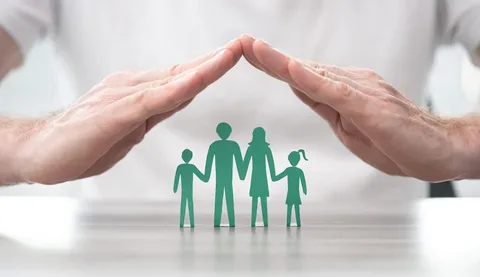 Two hands forming a protective roof over a green paper cutout of a family to represent the financial security of a life insurance policy