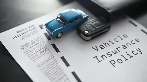 A blue toy car and a car key resting on top of a vehicle insurance policy document to illustrate auto insurance coverage options.