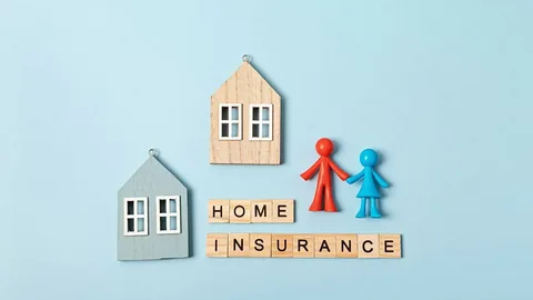 Wooden block letters spelling home insurance next to two small toy houses and figurines of a couple on a light blue background.